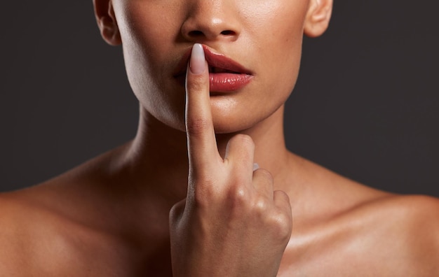 Foto labios de los dedos y belleza con una mujer modelo en estudio sobre un fondo gris para el cuidado de la piel o cosméticos maquillaje de manos y boca con una mujer tocándose el labio para promocionar un lápiz labial o un producto cosmético