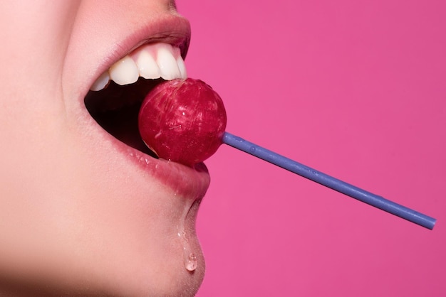 Lábios femininos fechados com gloss rosa segurando na boca pirulito vermelho doces lábios pirulito rosto de mulher