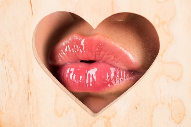 Foto labios en forma de corazón. labio rojo con brillo de labios brillante. lengua y sexy. de cerca, macro con hermosas bocas. beso sexy, labios seductores sensuales de una mujer joven. salón de belleza y cosmética.