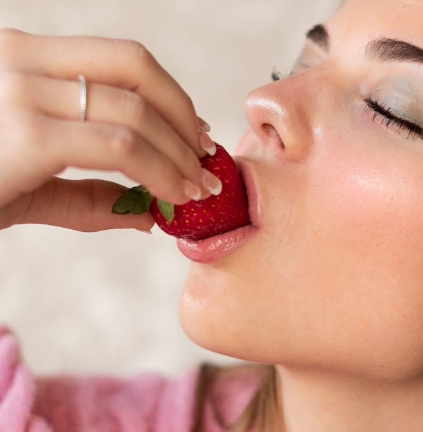 Lábios sensuais de jovem adolescente com pele branca lisa, comendo um delicioso morango vermelho