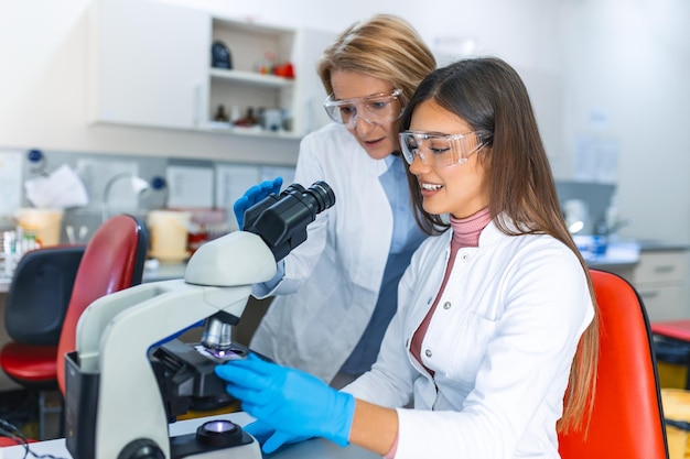 Laboratorio de Ciencias Médicas Hermoso Científico Mirando Bajo Microscopio Hace Análisis de Muestra de Prueba Jóvenes Especialistas Utilizando Equipos de Tecnología Avanzada