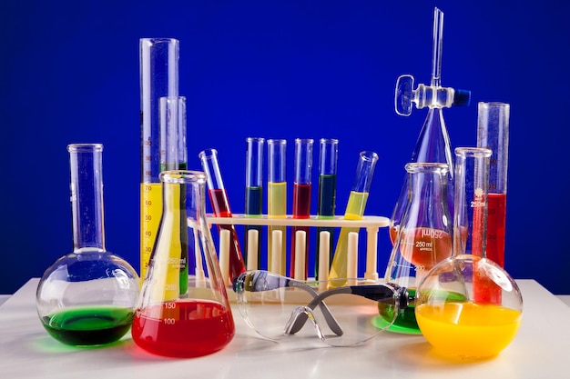 Laboratório de química com produtos químicos coloridos em uma mesa sobre fundo azul. Vidraria e equipamentos de biologia