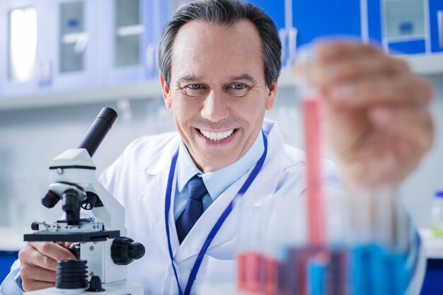 Laboratório moderno. homem inteligente positivo e encantado vestindo jaleco e trabalhando com amostras de teste enquanto está no laboratório