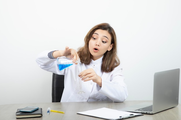 Laborforscherin, die am schreibtisch sitzt und medizinische glasflasche mit blauer flüssigkeit hält. Foto in hoher Qualität