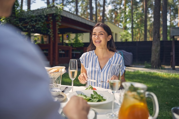 lachende Dame, die mit einem gutaussehenden Mann am Esstisch sitzt, während sie das warme Wetter auf dem Land genießt?