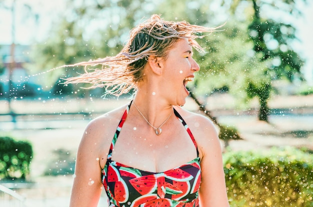 Lachende emotionale blonde Frau mit nassen Haaren, die Wasserspritzer macht. Urlaub, Glück, Spaß