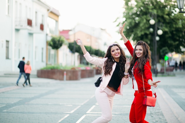 Lachende Frauen in sportlich-schicken Anzügen und Handtaschen auf der Straße.