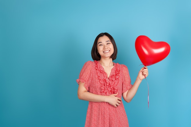 lachende, fröhliche junge asiatische Frau hält einen fliegenden roten herzförmigen Ballon