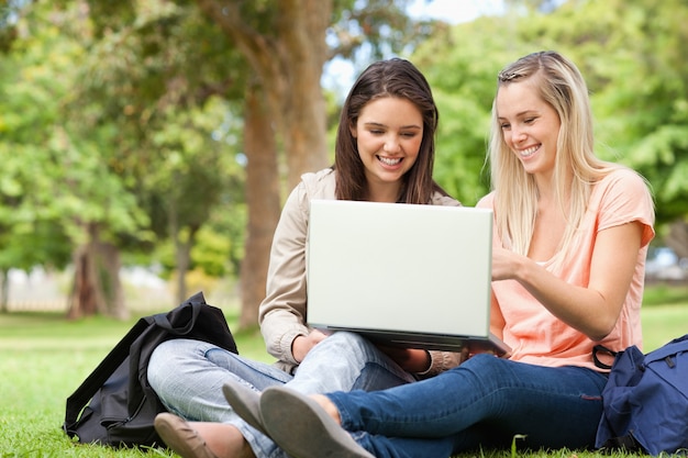 Lachende Jugendliche, die bei der Anwendung eines Laptops sitzen