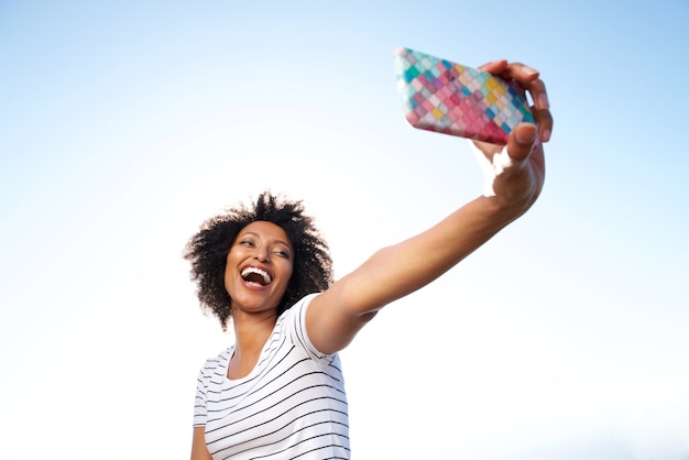 Lachende junge Afroamerikanerfrau, die draußen selfie mit intelligentem Telefon nimmt