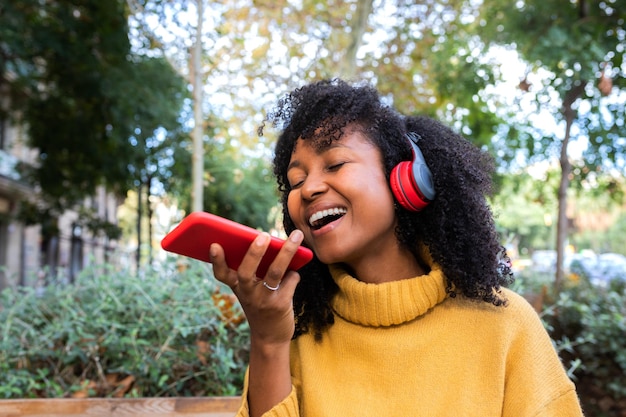 Lachende junge Afroamerikanerin, die eine Sprachnachricht mit dem Handy sendet. Lifestyle- und Technologiekonzept.