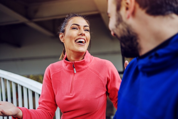 Lachende junge Fit-Sportlerin, die mit ihrem männlichen Freund spricht und Spaß hat, nachdem sie im Freien gelaufen ist. Konzept des städtischen Lebens.