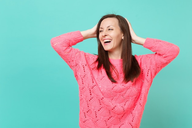 Lachende junge Frau in gestricktem rosa Pullover, der sich an den Kopf klammert, isoliert auf blau-türkisem Wandhintergrund, Studioporträt. Menschen aufrichtige Emotionen, Lifestyle-Konzept. Kopieren Sie Platz.