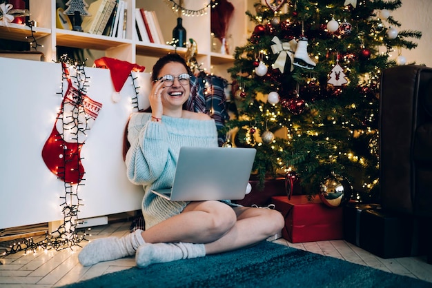 Lachende junge Frau mit Laptop im geschmückten Haus zu Weihnachten