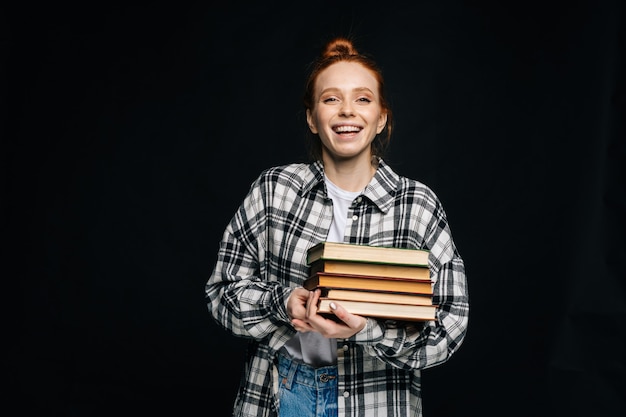 Lachende junge Studentin, die Bücher hält und in die Kamera schaut