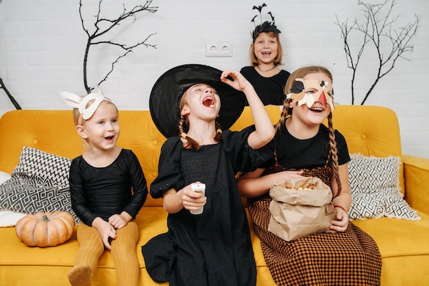 Foto lachende kinder, die für halloween gekleidet sind, sitzen auf der couch und schauen sich lustige cartoons an