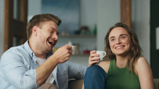 Lachende Liebhaber Kaffeetassen, die zu Hause in der Nähe stehen, sorglose Ehegatten, die Spaß haben