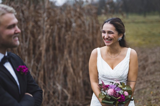 Lachende türkische Braut im ärmellosen Hochzeitskleid, die ihren Mann während des Herbst-Fotoshootings im Freien auslacht Beste Freunde als Ehepartner