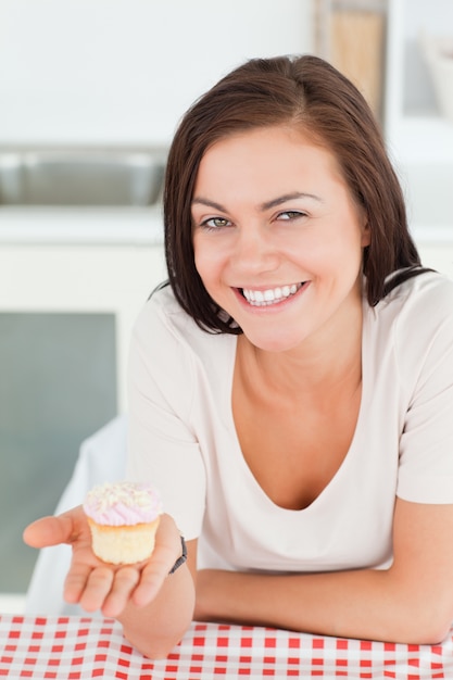 Lachender Brunette, der einen kleinen Kuchen zeigt