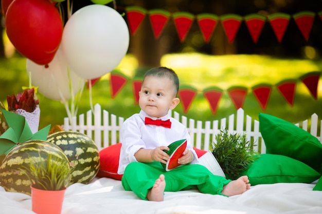 Lachender Junge 1-2 Jahre alt, der draußen Wassermelone isst. Sommerfestkonzept