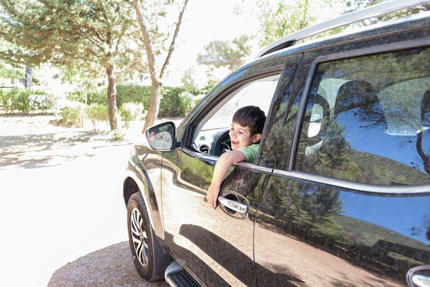 Lachender Junge, der aus dem Autofenster schaut Glückliches Kind auf dem Rücksitz des Autos, das den Blick aus dem Fenster genießt Das Konzept der Freiheit, Schulferien oder Feiertage