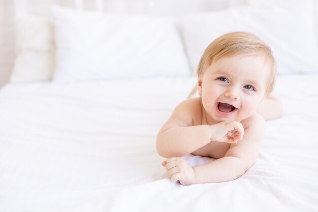Lachender oder lächelnder Babyjunge blond mit großen Augen Nahaufnahme oder Porträt in einer Krippe zu Hause das Konzept von Kinderwaren und Accessoires