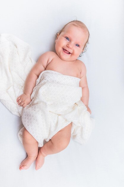 Lachendes Baby, das auf einem weißen Laken liegt und mit einem Wolltuch bedeckt ist