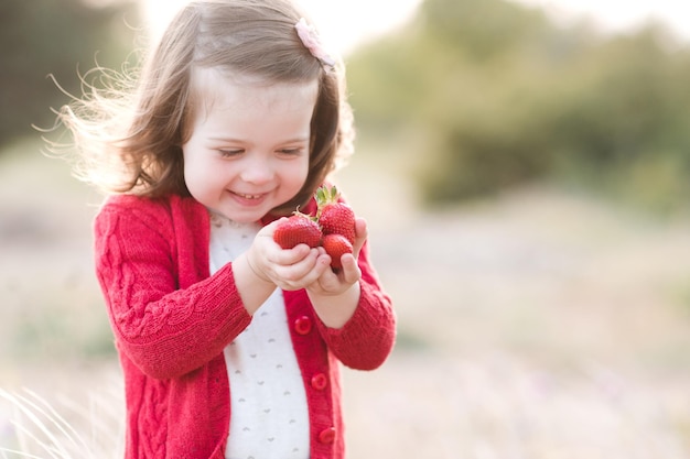 Lachendes Baby, das frische rote Erdbeere hält