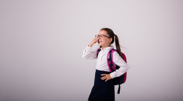 Lachendes brünettes Schulmädchen in Uniform und Brille auf weißem Hintergrund mit Platz für Text