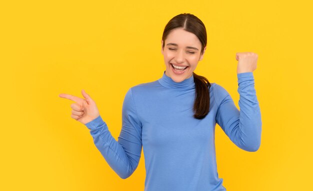 Lachendes Frauenporträt, das mit dem Finger auf den Erfolg des gelben Hintergrunds des Kopierraums zeigt