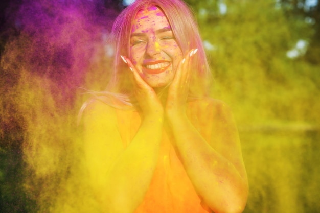 Foto lachendes junges model posiert mit explodierender gelber farbe beim sommer-holi-festival