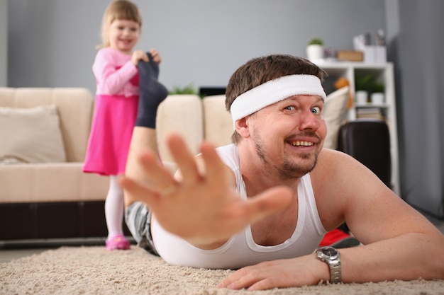 Lachendes kleines Mädchen, das Papas Bein auf den Boden zieht