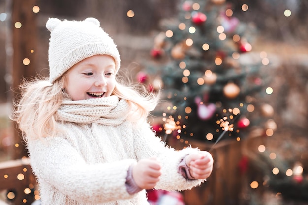 Lachendes kleines Mädchen hält Spakler über Weihnachtsbeleuchtung
