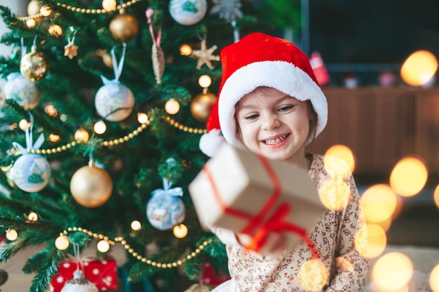 Lachendes kleines Mädchen mit Geschenkbox nahe dem Weihnachtsbaum