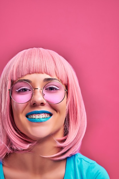 Lachendes Mädchen mit rosa Haaren, blauen Lippen und Sonnenbrille Stilvolle Haarfarbe Trend Isolierter rosa Hintergrund Vertikales Foto