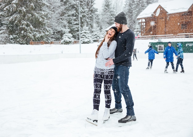 Lachendes Paar in Schlittschuhen, das draußen mit Schnee im Hintergrund spricht