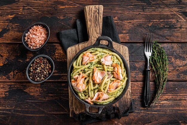 Lachs-Bucatini-Nudeln mit cremiger Spinatsauce und Fischfilet. Hölzerner Hintergrund. Ansicht von oben.