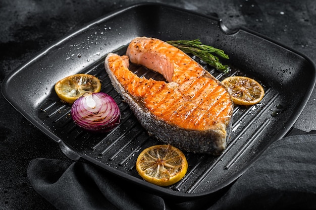 Lachs-Fisch-Steak gegrillt auf einer Grillpfanne mit Kräutern. Schwarzer Hintergrund. Ansicht von oben.