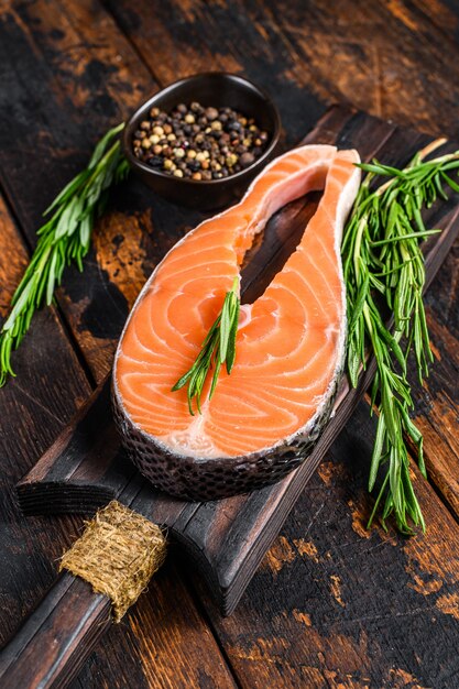 Lachs rohes Fischsteak zum Kochen auf einem Schneidebrett vorbereitet. Dunkler hölzerner Hintergrund. Draufsicht.