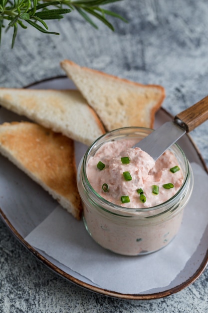 Lachs und Weichcremekäse im Glas verteilen. Lachs Rillettes, Mousse, Pastete und Toast auf grauem Hintergrund