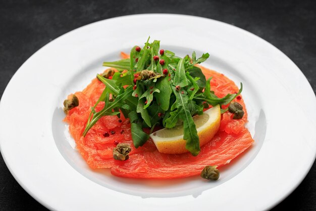 Lachscarpaccio auf einem Teller mit Zitrone auf Beton