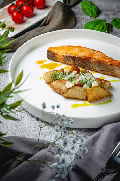 Lachsfilet gebacken mit rustikalen Kartoffeln auf süßen Birnen gefüllt mit edlem Käse mit einer Sauce aus reifen Orangen in einem Teller auf einem grauen Steintisch. Speisekarte