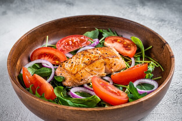 Lachsfiletsteaksalat mit grünen Blättern, Rucola, Avocado und Tomate in einer Holzplatte. Weißer Hintergrund. Ansicht von oben.