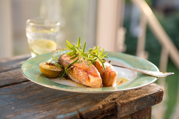 Lachsfischsteak mit Glas Wasser gegrillt, Abendessen. Gesundes Essen. Draufsicht Köstliche gebratene Lachsfiletgewürze auf natürlichem Gartenhintergrund.