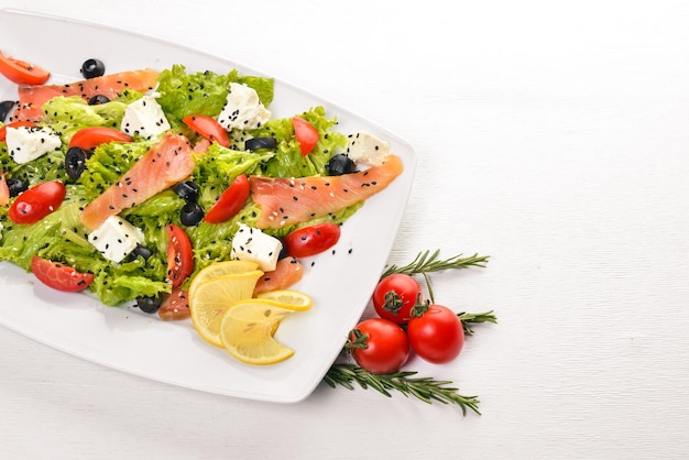 Lachssalat Feta-Käse-Salatblätter und frisches Gemüse auf dem Teller Auf einem hölzernen Hintergrund Ansicht von oben Freier Platz für Text