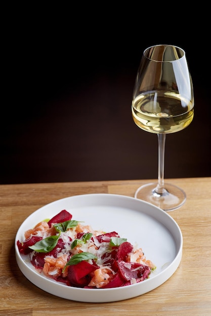 Lachssalat mit Rübenkäse und grünen Blättern auf Holztisch mit Glas Weißwein.