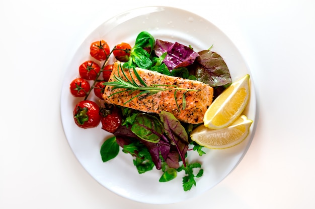 Lachssteak mit Salat, Kirschtomaten und Zitronenscheiben. Galadinner. Essen zum Mittagessen. Gegrillter roter Fisch. Gebackener Lachs im Ofen