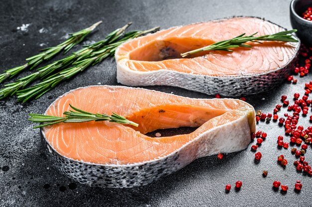 Lachssteaks mit Rosmarin und rosa Pfeffer. Roher Bio-Fisch. Schwarzer Raum. Draufsicht