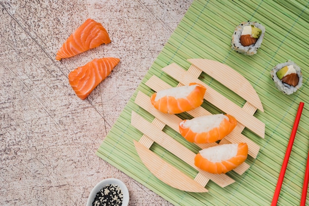 Foto lachssushirollen auf kreisförmiger hölzerner platte auf grünem placemat mit essstäbchen und samen des indischen sesams