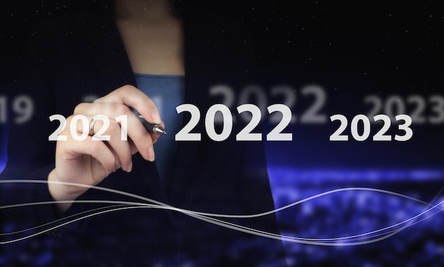 Ladejahr 2021 bis 2022. Startkonzept. Hand, die einen digitalen Grafikstift hält und ein digitales Hologramm 2022-Zeichen auf der Stadt dunkel unscharf zeichnet. Konzept für Vision 2021-2022. Geschäftsmann Willkommensjahr.